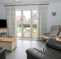 A living room with leather chairs a wooden coffee table a television and glass doors leading outside at Silversands in Filey