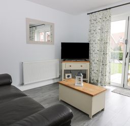 A living room with a black sofa a coffee table a television on a stand and glass doors at Silversands in Filey