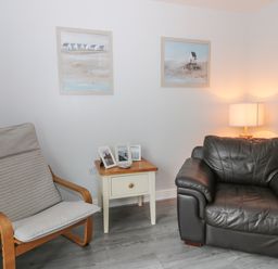 A corner with a wooden armchair with cushions a black leather armchair a small wooden side table with photo frames and a lamp Silversands Filey