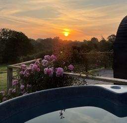 A hot tub on a deck with flowers and a sunset at Embden Pod at Banwy Glamping Llanfair Caereinion