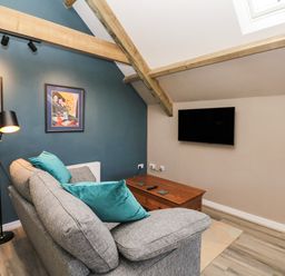 A living room with a gray sofa with blue cushions a wooden coffee table a floor lamp wall art and a wall-mounted TV at Cherrywood Barn in South Petherton