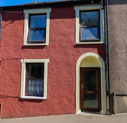 The exterior of a two story house with a red facade two windows and a door at Ty Coch y Castell in Pembroke