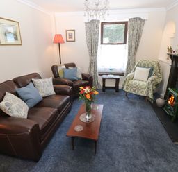 A living room with leather sofas a wooden coffee table with flowers and a stove at Ty Coch y Castell in Pembroke
