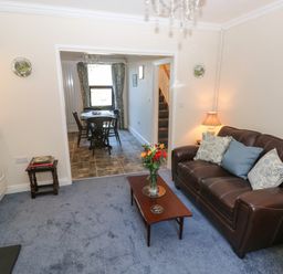 A living room with a brown leather sofa and a wooden coffee table next to a dining area with a table and chairs at Ty Coch y Castell in Pembroke