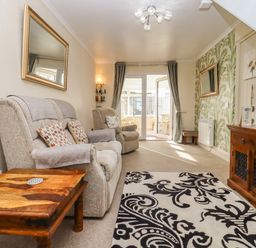 A living room with upholstered armchairs wooden table patterned rug and a television at Molly's Bit in Church Westcote near Bourton-On-The-Water