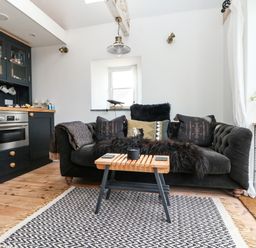 A living area with a black sofa and cushions a wooden coffee table and a kitchen unit with an oven at Rocket Cart House in Lizard