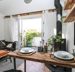 A dining table with plates and bowls in a living room with an open door leading outside at Rocket Cart House in Lizard