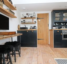 A kitchen with black cabinets wooden countertops wooden shelves and stools with black fur covers at Rocket Cart House in Lizard