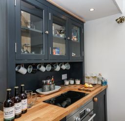 A kitchen counter with bottles mugs and glasses next to a stove at Rocket Cart House in Lizard