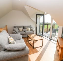 A seating area with two gray sofas a wooden coffee table a flat screen tv on a wooden stand and glass doors leading to a balcony at Glowty Brynbedw in Efailwen
