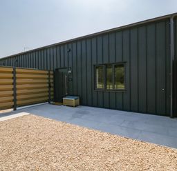 An outdoor area with a black building wall a door a window gravel ground and beige fencing at Tilia Barn in Wincanton