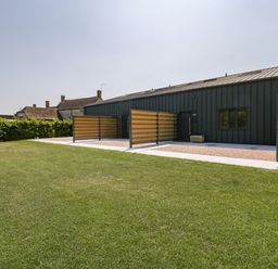 A modern building with dark siding and wooden slatted panels on a lawn at Tilia Barn in Wincanton