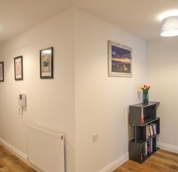 A hallway with framed pictures on the wall a small bookshelf with books and a vase of flowers at Nautical Breeze in Weymouth
