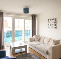 A living room with a white sofa, wooden coffee table, blue armchair, TV on a stand, and glass doors leading to a balcony at Nautical Breeze in Weymouth