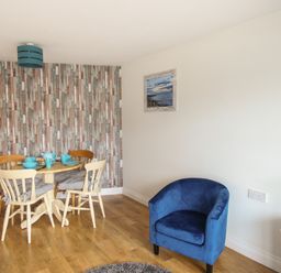 A dining area with wooden table and chairs and a blue armchair in a room at Nautical Breeze in Weymouth