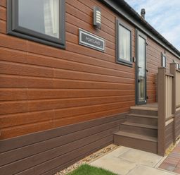 Exterior view of a building with wooden siding steps leading to a door and windows at Sea Holly Lodge in Runswick Bay