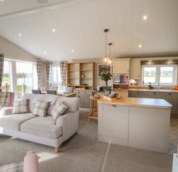An open plan living room and kitchen with plaid cushions and curtains at Sea Holly Lodge in Runswick Bay