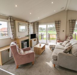 A living room with sofa armchairs coffee table and TV at Sea Holly Lodge in Runswick Bay