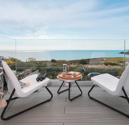 A balcony with two white chairs and a table with tea set overlooking the sea at Sea Sands in Praa Sands
