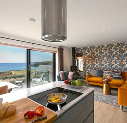An open kitchen and living room with a cooking island cutting board with bread and peppers and a sea view at Sea Sands in Praa Sands