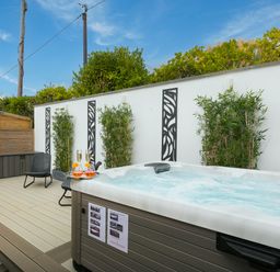 An outdoor patio with a hot tub champagne glasses two chairs plants and decorative wall panels at Sea Sands in Praa Sands