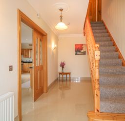 An entry hallway with a wooden staircase carpeted stairs a small table with flowers and a painting on the wall at Redford View Culdaff County Donegal