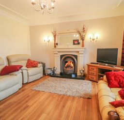 A living room with beige sofas red cushions a fireplace a television on a wooden stand and red curtains at Redford View in Culdaff County Donegal