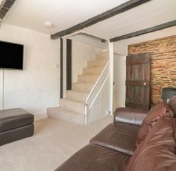 A living room with a leather sofa a ottoman a wall mounted television and stairs at Pixie Cottage in Looe