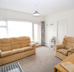 A living room with two beige sofas a small side table with books and a wooden table with flowers at 14 Siesta Mar in Mundesley