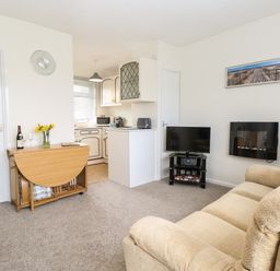 A living room with sofas a wall-mounted fireplace a TV and a drop-leaf dining table next to a kitchen at 14 Siesta Mar in Mundesley