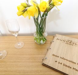 A wooden table with yellow flowers in a glass vase two empty wine glasses and a guest information pack at 14 Siesta Mar in Mundesley