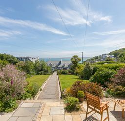A garden with lawn and flower beds a pathway and wooden chairs overlooking houses and the sea at 6 Albany Terrace in St Ives
