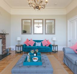 A living room with a blue sofa pink cushions gray armchair gray ottoman and a fireplace at 6 Albany Terrace in St Ives