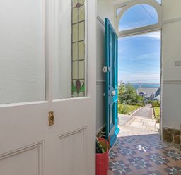An open front door with stained glass panel and tiled floor looking out to a garden path and sea view at 6 Albany Terrace in St Ives