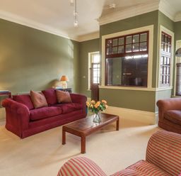 A living room with red sofas a wooden coffee table with flowers and green walls at Lion House in Moretonhampstead