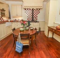 A kitchen with a wooden table set with dishes and flowers and cream cabinets with a stove and red and white tiled backsplash at Lion House in Moretonhampstead