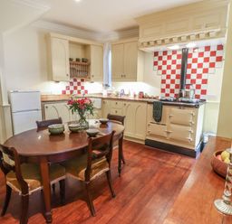 A kitchen with a wooden dining table and chairs beige cabinets and a white stove with red and white tiled backsplash at Lion House in Moretonhampstead