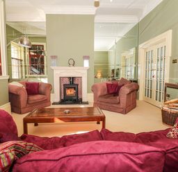 A living room with striped armchairs a red sofa a wooden coffee table and a fireplace at Lion House in Moretonhampstead