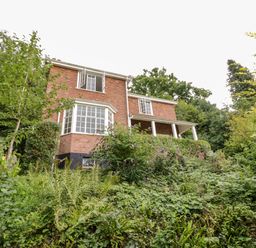A brick house with white framed windows surrounded by green vegetation and trees at Tor Cottage in Colwall Herefordshire