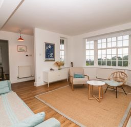 A living room with chairs and a table on a rug and large windows at Tor Cottage in Colwall Herefordshire