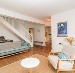 A living room with a blue sofa a white armchair a round white table a rug wooden flooring and a staircase at Tor Cottage in Colwall Herefordshire