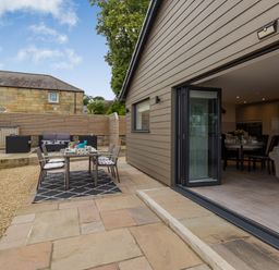 An outdoor patio area with a dining table and chairs next to an open door leading to an indoor dining and living space at Secret Kingdom Cottage in Warkworth