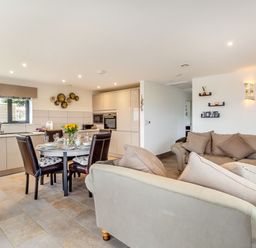 An open plan kitchen and living area with a dining table set for four and two sofas at Secret Kingdom Cottage in Warkworth