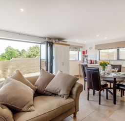 An open plan kitchen and dining area with a sofa and round dining table set with dishes at Secret Kingdom Cottage in Warkworth