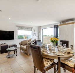 A living and dining area with a round table set for four people a sofa a wall-mounted television and a cupboard at Secret Kingdom Cottage in Warkworth