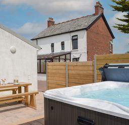 An outdoor patio with a hot tub and wooden picnic table near a white building and a brick house at Silver Crooks in Trewyn Nr Holsworthy