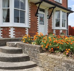A concrete curved staircase leading to a white door with stained glass and orange flowers in the garden of a red brick house at Silver Crooks in Trewyn Nr Holsworthy