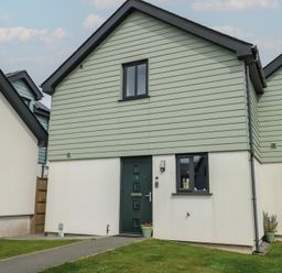 Front exterior of a modern two-story house with green upper cladding white lower walls a green door and windows at 4 Parc Delfryn in Brynteg near Benllech