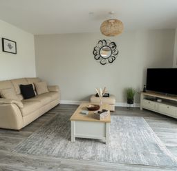 A living room with a beige sofa a coffee table a TV on a stand and a round wall mirror at 4 Parc Delfryn in Brynteg near Benllech
