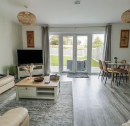 A living room with a television on a stand a coffee table a dining table with four chairs and glass doors leading to a garden at 4 Parc Delfryn Brynteg near Benllech